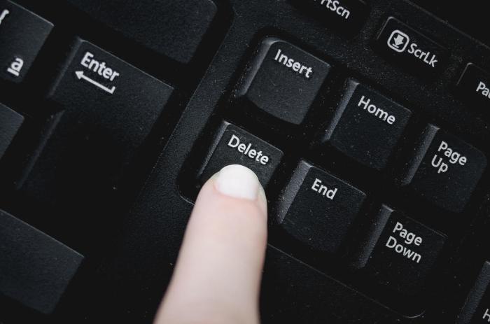 Finger over the delete key from a dusty black keyboard